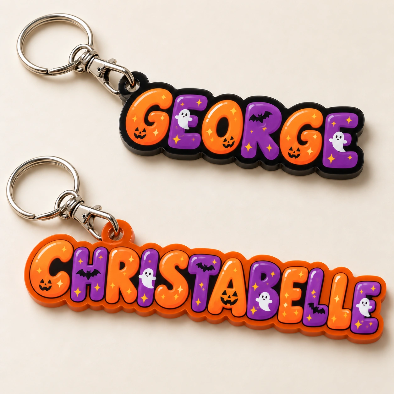 Halloween name-keyring design preview with connected orange and purple bubble letters, printed pumpkins, ghosts and bats: GEORGE on black acrylic and CHRISTABELLE on orange acrylic.