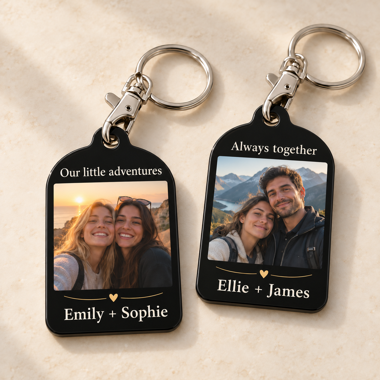 Two black acrylic photo keyrings with ivory text above and below portraits: Emily + Sophie and Ellie + James. Silver-colour lobster clasps clip directly through the tags and connect to round split rings.
