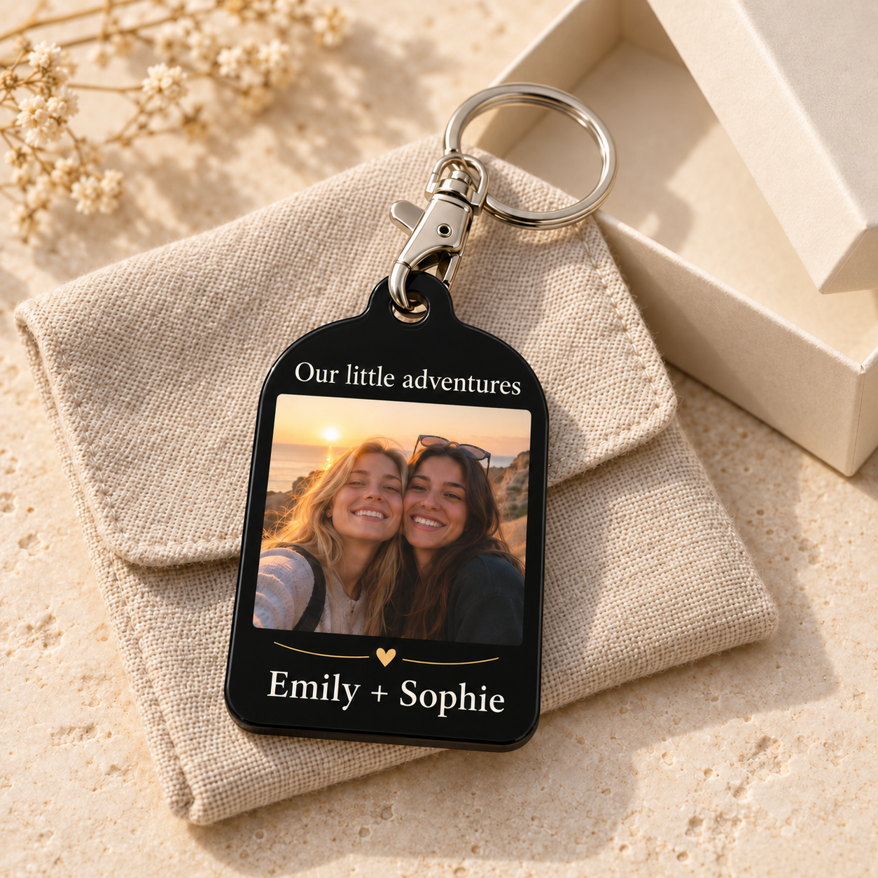 Emily + Sophie black acrylic photo keyring on oatmeal linen beside a cream gift box, with Our little adventures above the friends' photo and ivory names below.