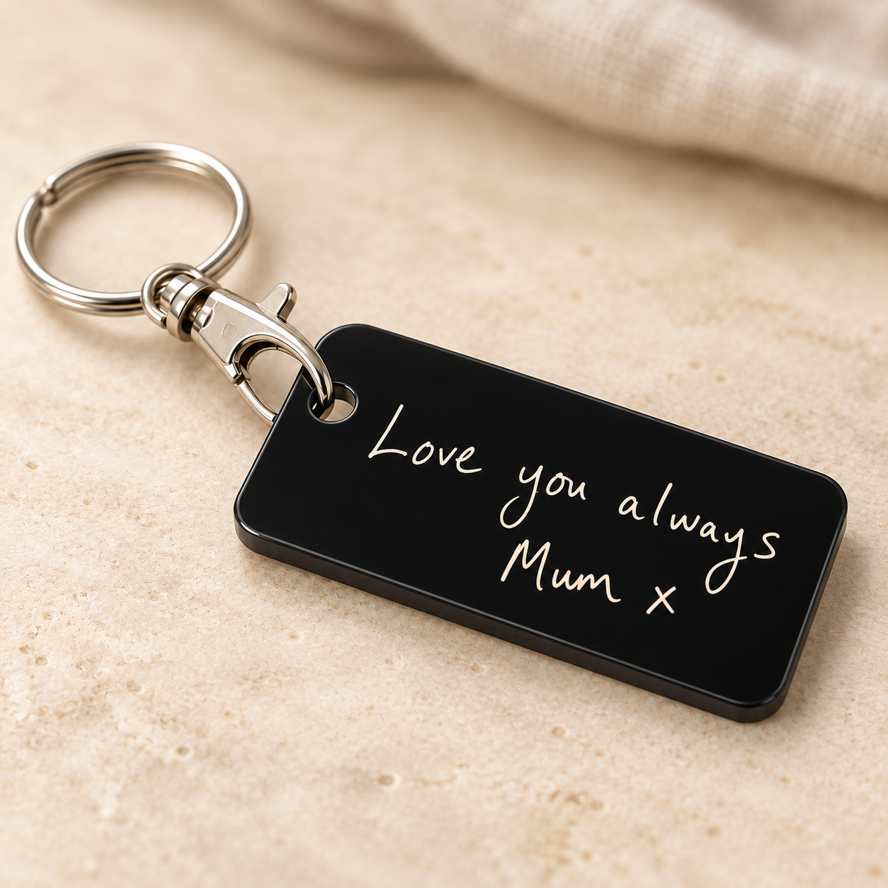 Close view of a black acrylic handwritten-note keyring, its slim dark edge and silver-tone lobster clasp clipped through the hole, with a split ring attached at the other end.