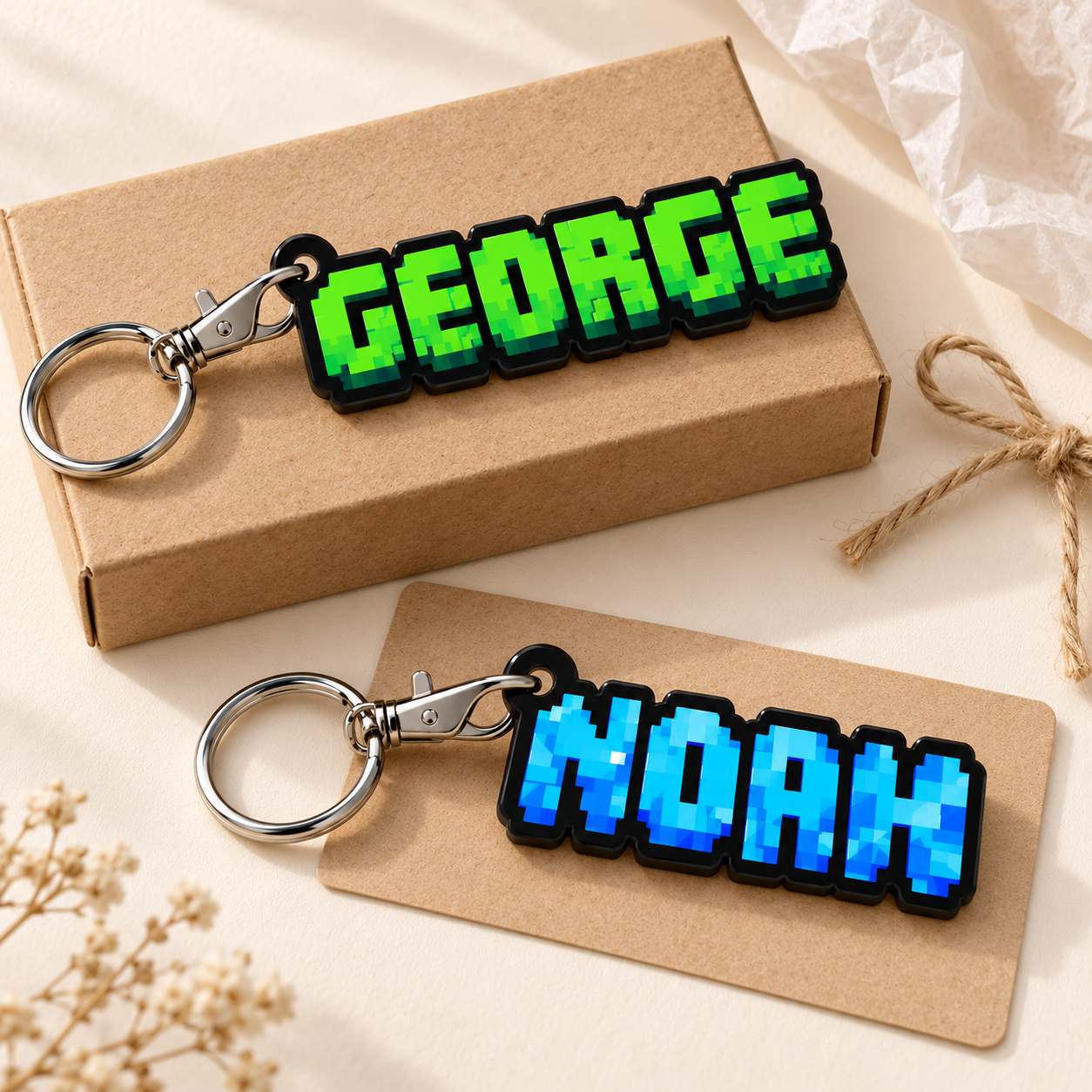 Digital gift mockup of green GEORGE and blue NOAH personalised pixel-name acrylic keyrings beside plain kraft packaging and twine. Packaging shown as a styling prop.